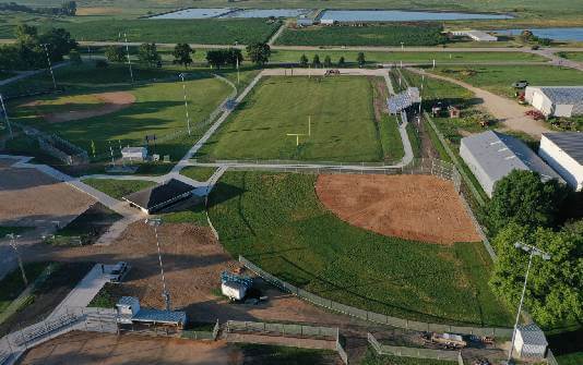 Aerial view of a sports complex featuring multiple baseball and soccer fields, surrounded by roads and greenery, under a clear sky.