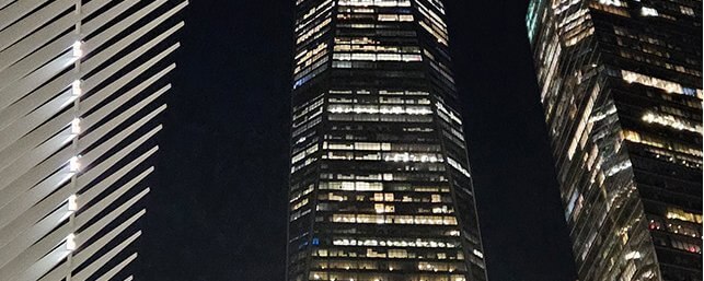 Night view of three illuminated skyscrapers against a dark sky, showcasing modern architectural design.