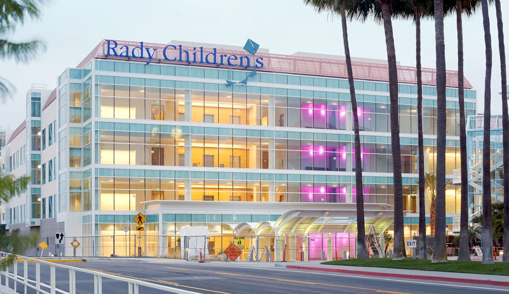 Rady Children's Hospital building with a modern glass facade, featuring illuminated windows and a prominent sign displaying its name.