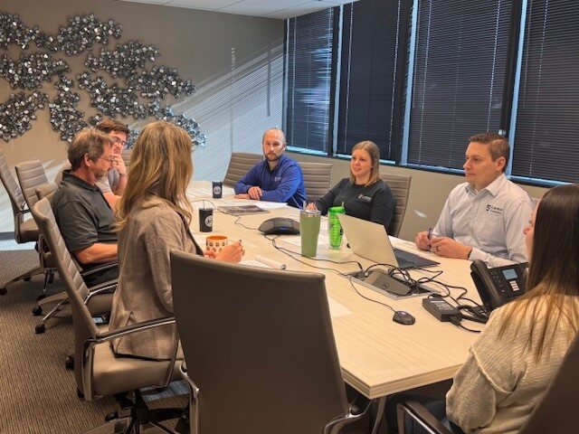 Larson Engineering team members engaged in a meeting around a conference table, with laptops and documents, in a modern office setting.