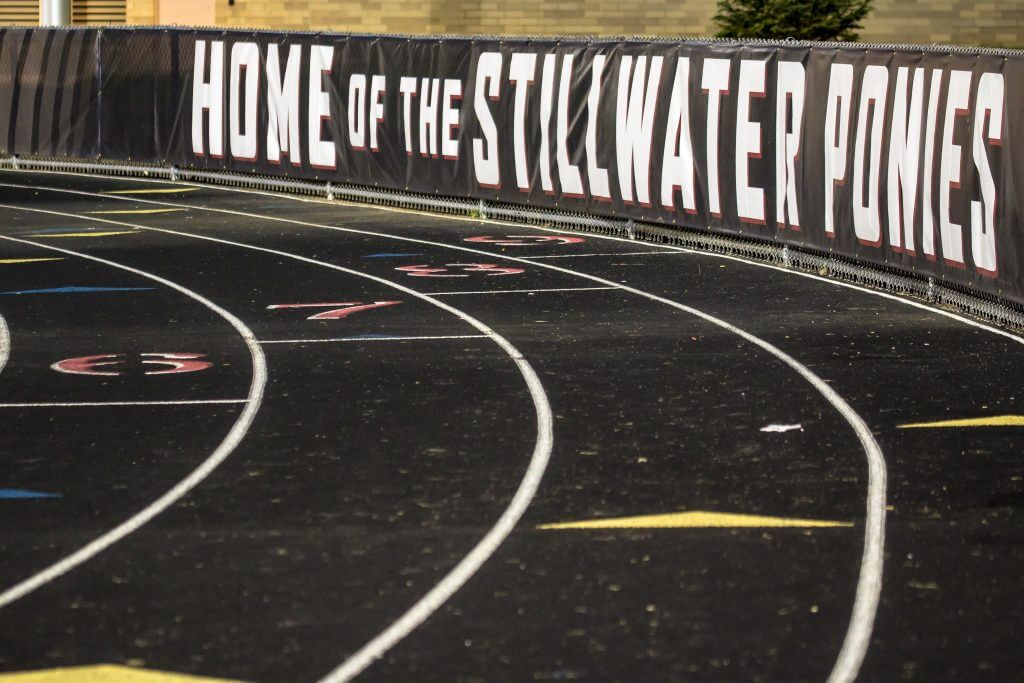 Running track with lanes and a banner reading "Home of the Stillwater Ponies" along the fence.