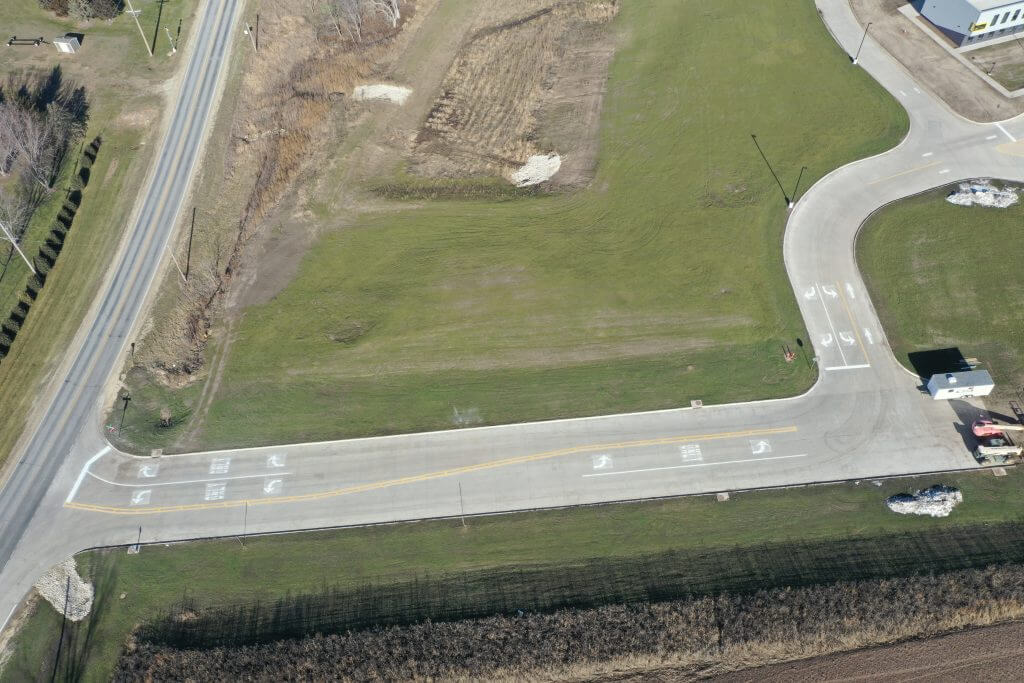 Aerial view of a road intersection near Waverly Shell Rock East Elementary, showing a curved road with marked lanes surrounded by grassy areas and fields.