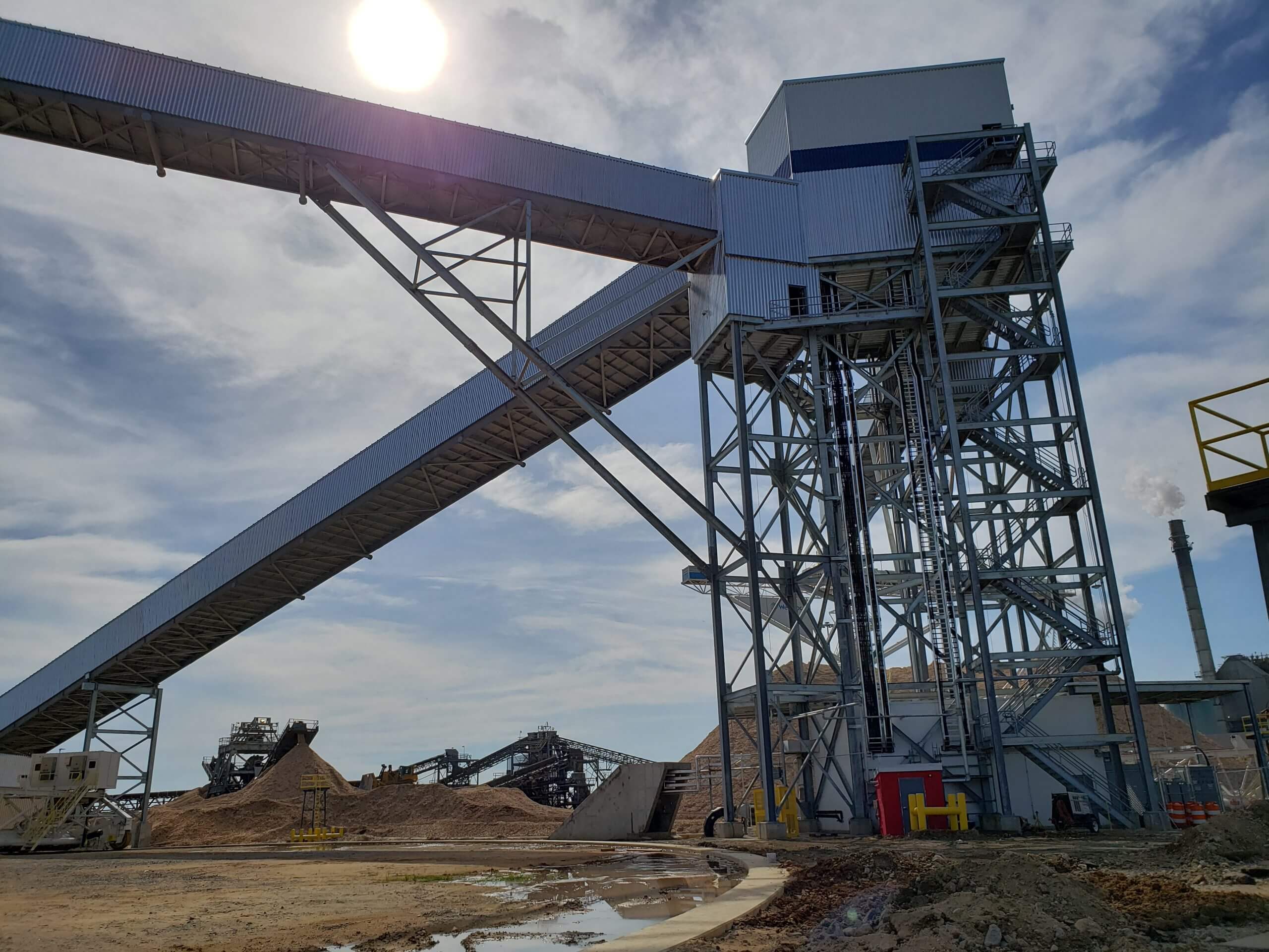 Industrial facility with a large steel structure featuring a conveyor belt system under a bright sky, highlighting civil and structural engineering.