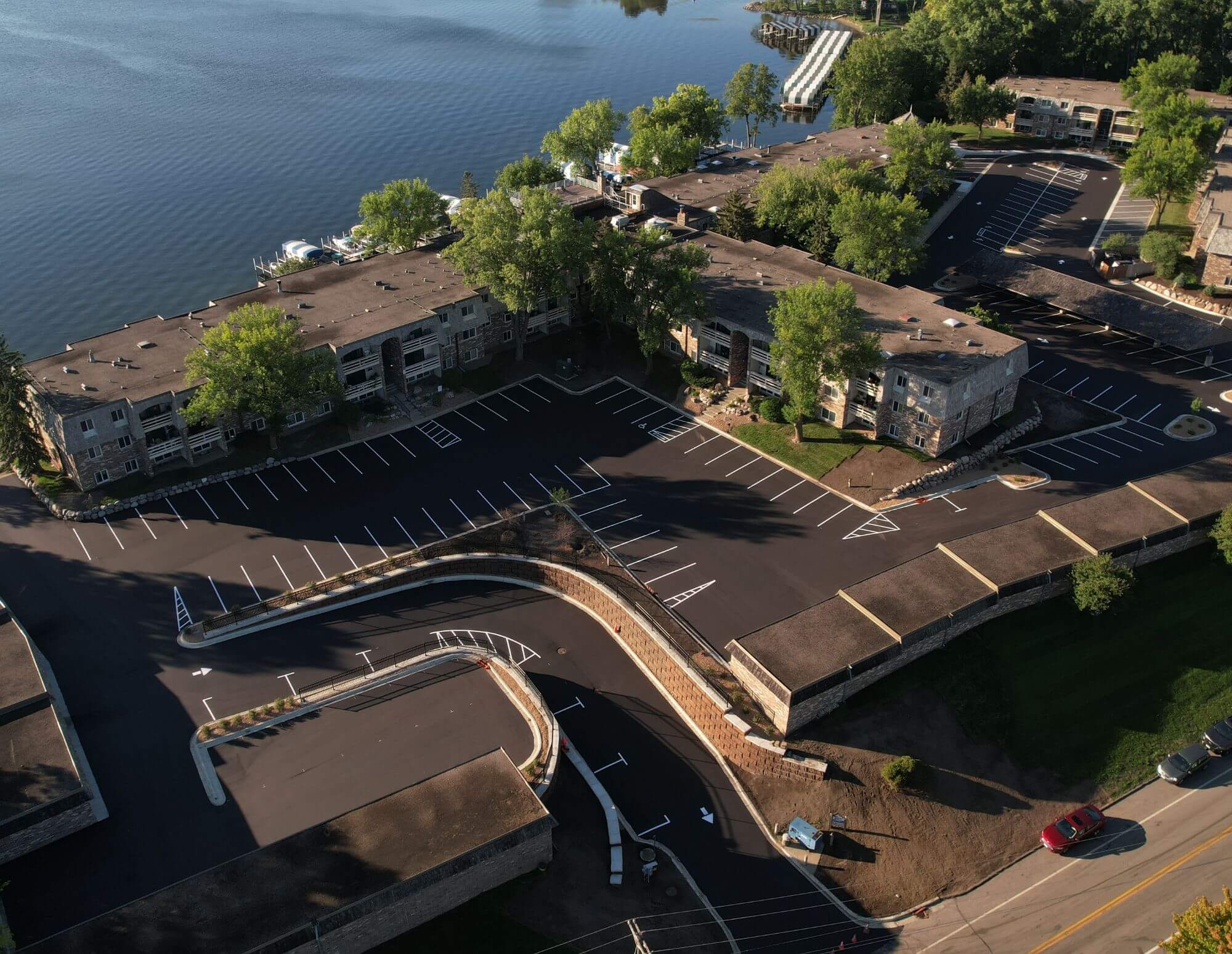 Aerial view of a newly paved parking area adjacent to a lake, surrounded by buildings and trees, illustrating civil engineering work by Larson Engineering.