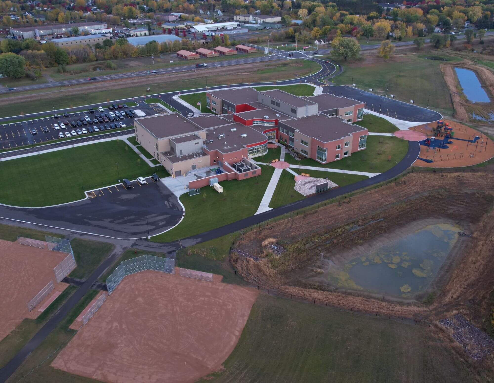 Aerial view of a large, modern educational facility with multiple connected buildings, surrounded by green lawns, parking areas, and sports fields, illustrating site design in civil engineering.