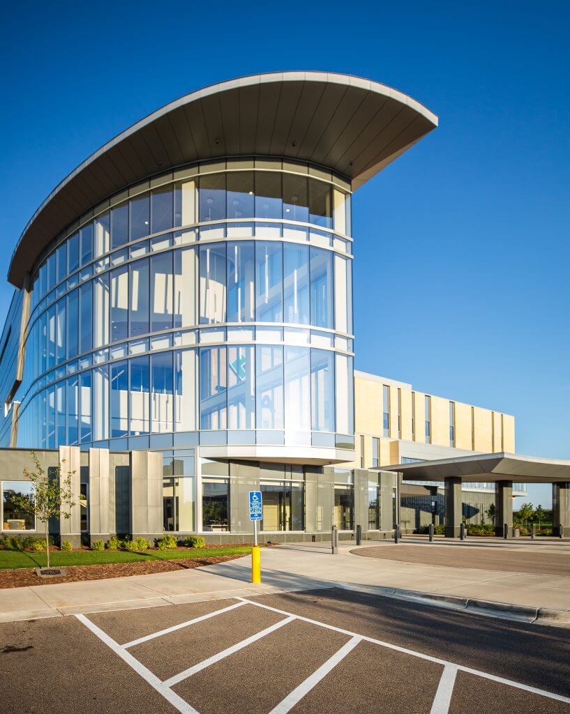 Modern commercial building with curved glass facade and metal roof, set against a clear blue sky.