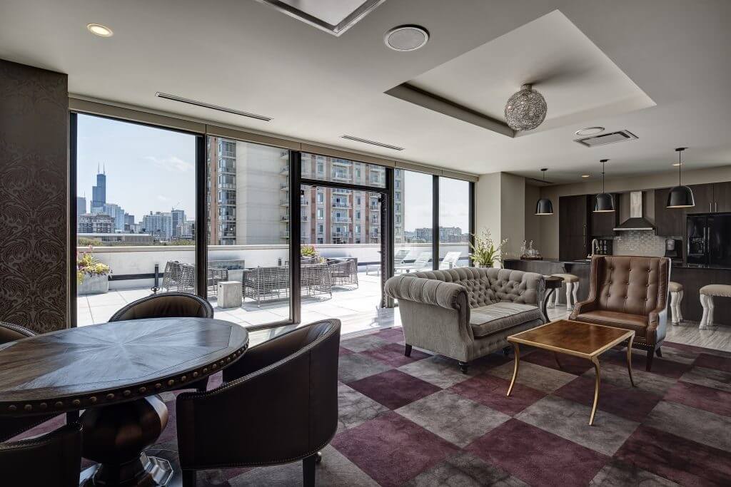Modern interior of a spacious living area with large windows overlooking a cityscape, featuring a seating area with sofas and a dining table, adjacent to a kitchen.