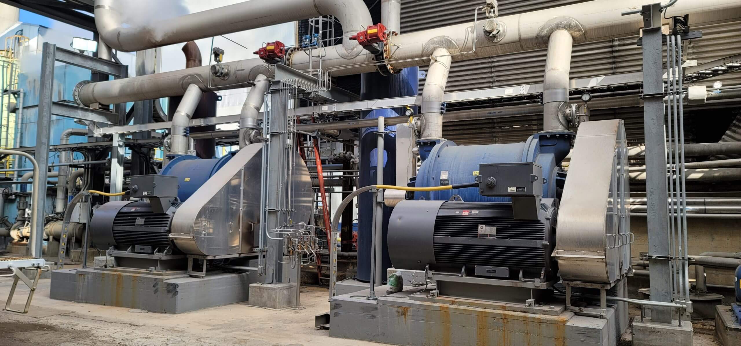 Industrial vacuum system with large blue and silver machinery, surrounded by interconnected pipes and metal structures in a facility setting.