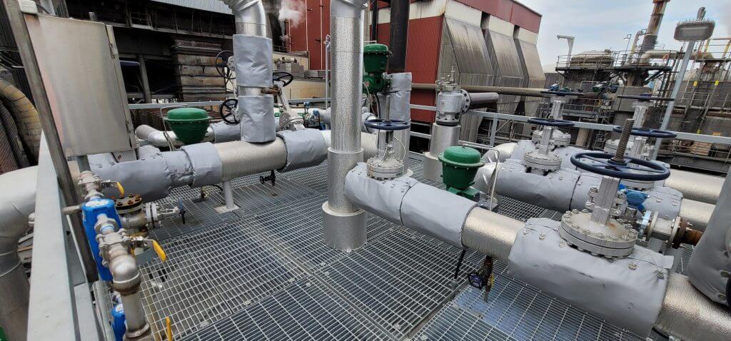 Condensate piping system with insulated pipes and valves on a metal grate platform at a paper facility, designed by Larson Engineering.