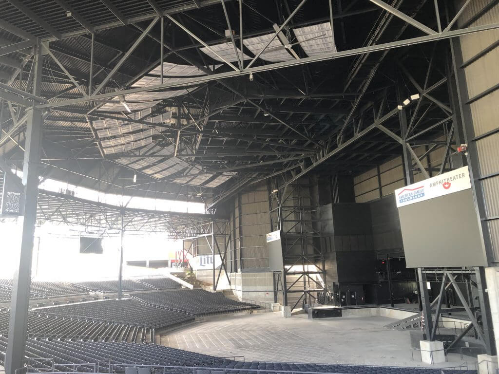 Interior view of the American Family Insurance Amphitheater, showcasing its expansive roof structure, seating area, and stage, with visible signs reading "American Family Insurance Amphitheater."