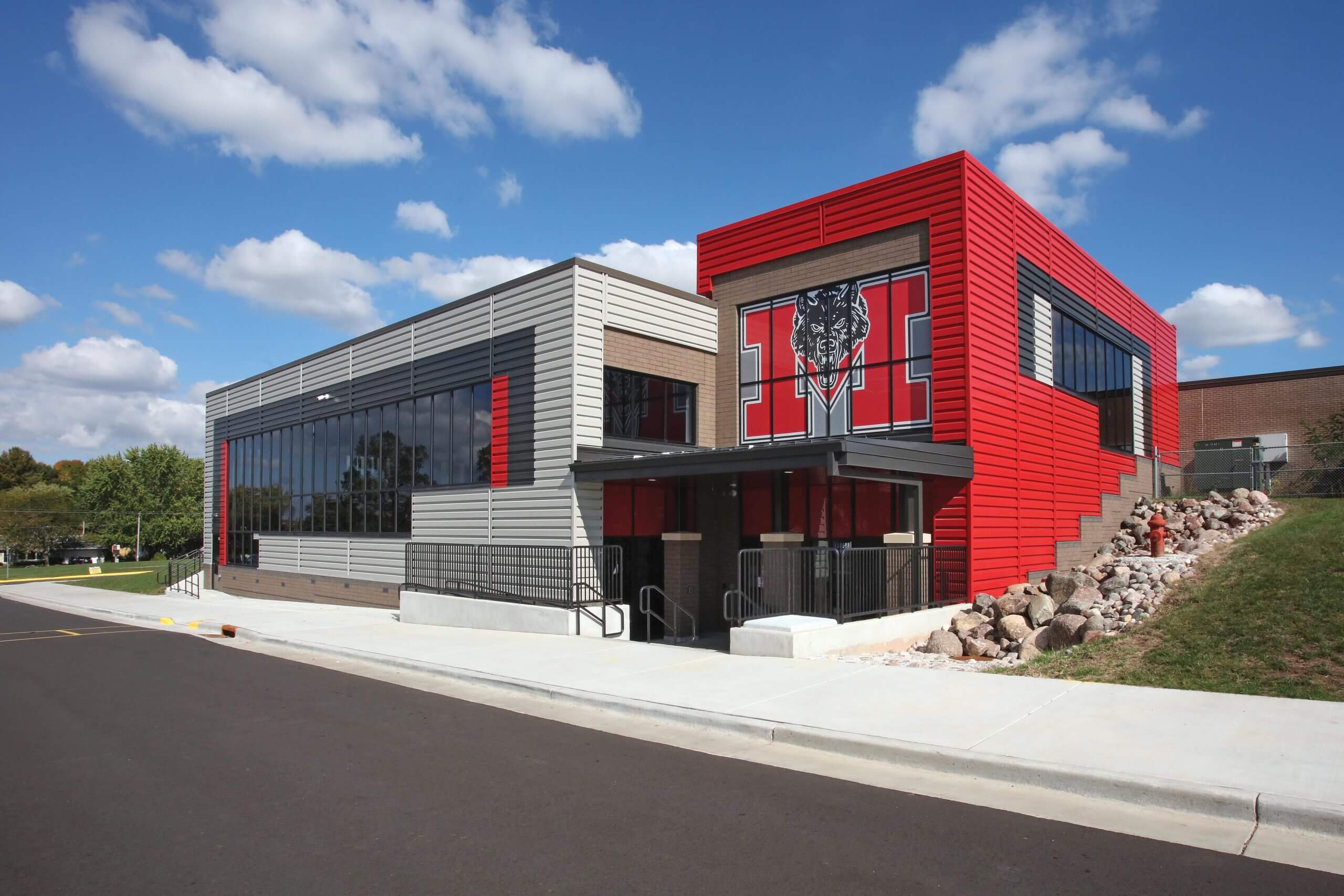Modern school building with red and gray exterior, featuring large windows and a prominent logo of a panther on the facade.