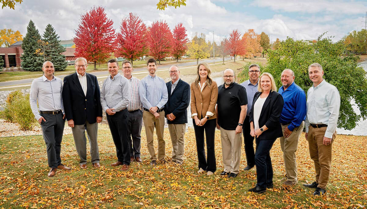 Group of Larson Engineering team members standing outdoors on a lawn with autumn trees in the background.